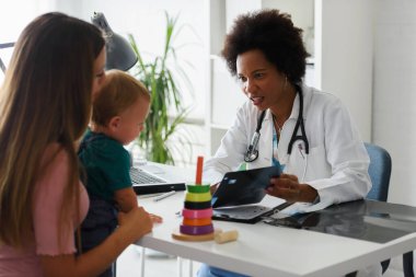 Afro-Amerikan çocuk doktoru. Çocuğu hastanede muayene ediyor. Annesi çocuğu hastanede. 