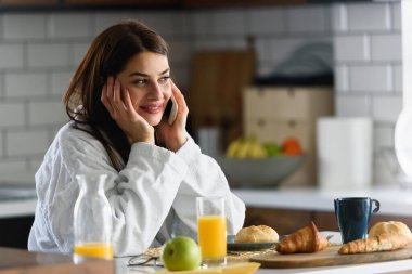 Bornozlu genç bir kadın sabah mutfakta akıllı telefon kullanarak uyandı.