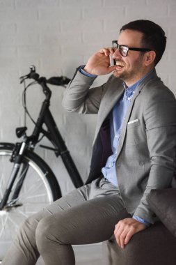 Takım elbiseli yakışıklı genç işadamı ve arka planda bisikleti olan gözlükler.