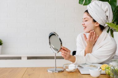 Kafasında havlu olan güzel genç bir kadın günlük cilt bakımını rutin hale getiriyor.