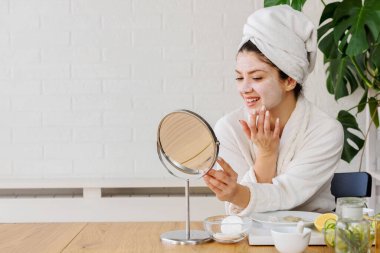 Kafasında havlu olan güzel genç bir kadın günlük cilt bakımını rutin hale getiriyor.