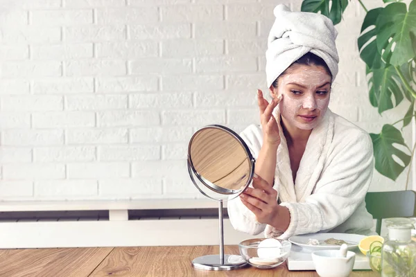 Kafasında havlu olan güzel genç bir kadın günlük cilt bakımını rutin hale getiriyor.