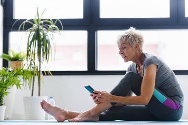 Son sınıf öğrencisi telefonuyla yoga minderinde oturuyor. 