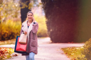Güzel genç bir kadın alışveriş torbalarıyla parkta yürüyor.