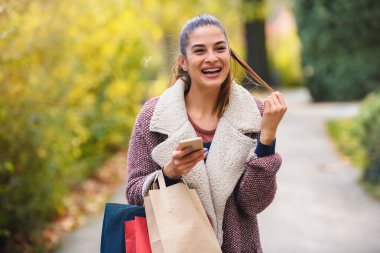 Güzel genç bir kadın alışveriş torbalarıyla parkta yürüyor.