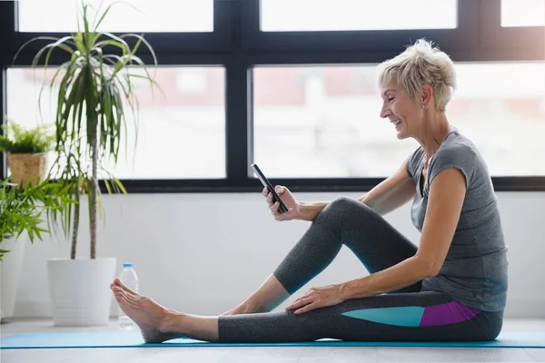 Seniorin Sitzt Mit Handy Auf Yogamatte — Stockfoto