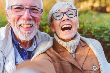Parkta bankta oturup selfie çeken mutlu çift.