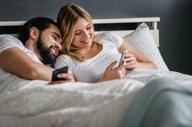 Mutlu çift sabahları yatakta uzanıp akıllı telefonlara bakıyor.