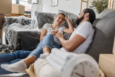 Mutlu genç çift yeni bir eve taşınıyor, yerde oturuyor ve kutlama yapıyorlar.