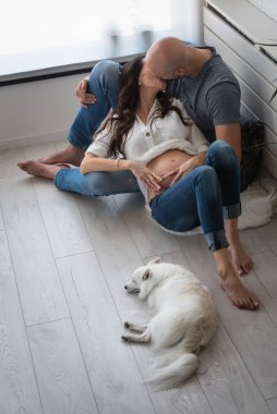 Oturma odasında kucaklaşan genç bir çift, yanlarında yatan bir köpek.