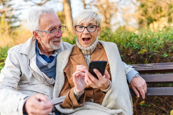 stock image senior couple sitting on bench in the park, making online order