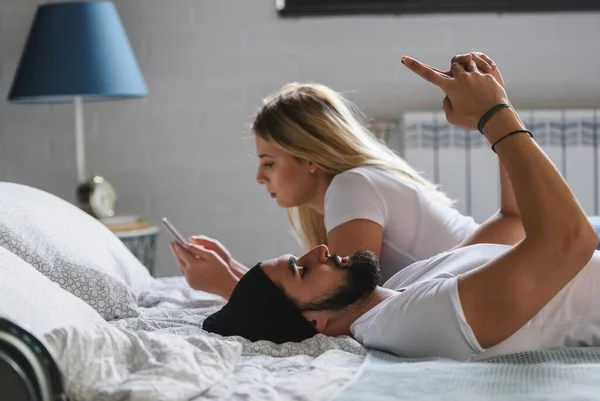 Расстроить Молодую Пару Лежа Кровати Используя Смартфоны — стоковое фото