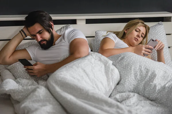 Üzgün Genç Bir Çift Yatakta Uzanıyor Akıllı Telefonlar Kullanıyor — Stok fotoğraf