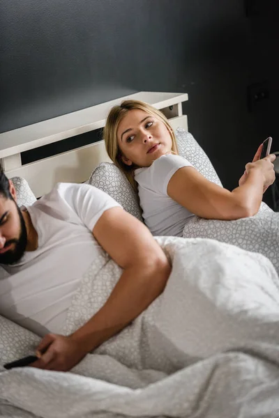 Üzgün Genç Bir Çift Yatakta Uzanıyor Akıllı Telefonlar Kullanıyor — Stok fotoğraf
