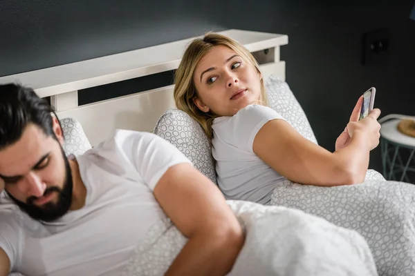 stock image upset young couple lying on bed and using smartphones