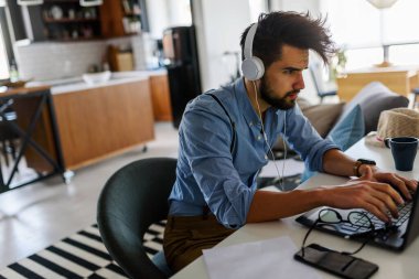 Genç ve yakışıklı bir adam evde dizüstü bilgisayar kullanıyor.