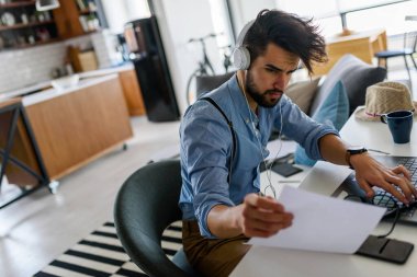 Genç ve yakışıklı bir adam evde dizüstü bilgisayar kullanıyor.