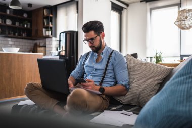 Genç adam dizüstü bilgisayar kullanıyor, evde çalışıyor.