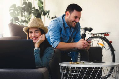 Genç çift kanepede oturup dizüstü bilgisayar kullanıyor.