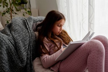 Oturma odasında kitabını okuyan genç bir kız.