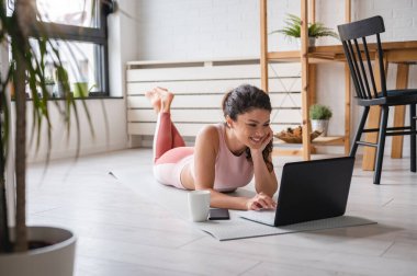 Laptop kullanan güzel genç bir kadın, online yoga dersleri alıyor. 
