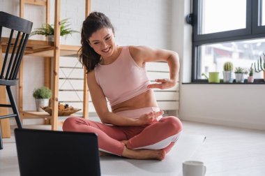 Laptop kullanan güzel genç bir kadın, online yoga dersleri alıyor. 
