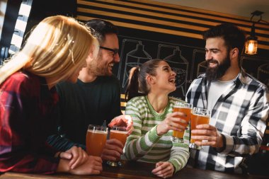 Bir grup genç arkadaş barda bira içip kadeh kaldırıyorlar.