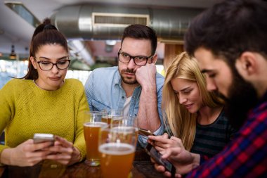 Arkadaşlar barda akıllı telefonlarla bira içiyorlar.