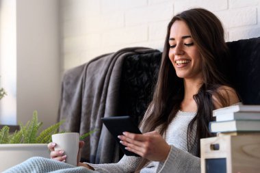 Tablet kullanarak evde kitap okuyan güzel bir kadın.