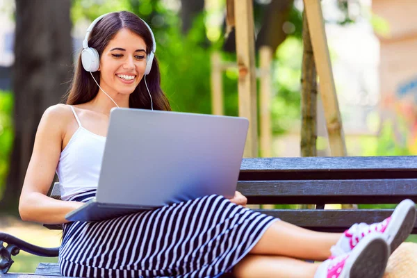 stock image young beautiful woman sitting on a bench and listening to music with headphones 
