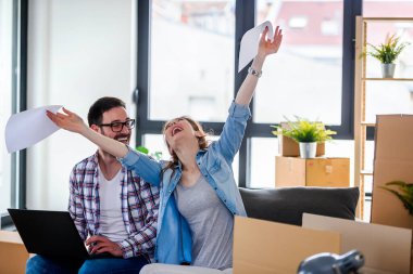 Mutlu genç çift dizüstü bilgisayar kullanıyor, yeni evine taşınıyor.