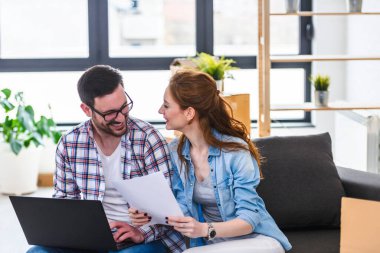 Mutlu genç çift dizüstü bilgisayar kullanıyor, yeni evine taşınıyor.