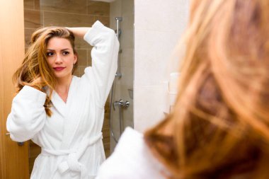 Güzel genç bir kadın hazırlanıyor, banyoda aynaya bakıyor.