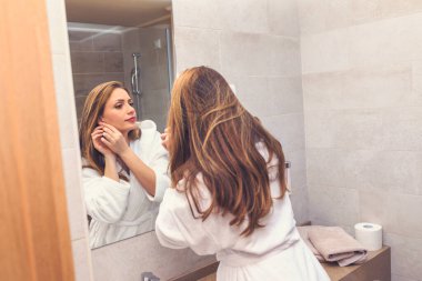 Güzel genç bir kadın hazırlanıyor, banyoda aynaya bakıyor.