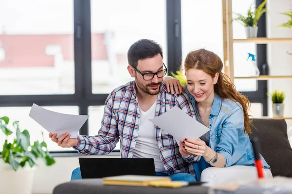 Mutlu genç çift dizüstü bilgisayar kullanıyor, yeni evine taşınıyor.
