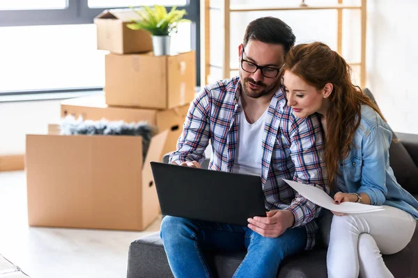 Mutlu genç çift dizüstü bilgisayar kullanıyor, yeni evine taşınıyor.