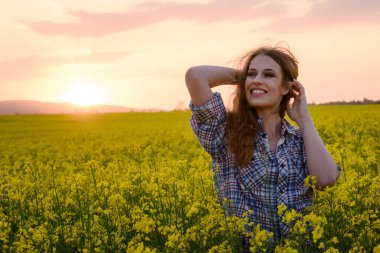Gün batımında kanola sahasında poz veren güzel bir kadın
