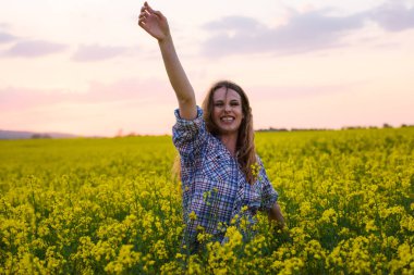 Gün batımında kanola sahasında poz veren güzel bir kadın