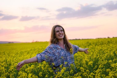 Gün batımında kanola sahasında poz veren güzel bir kadın