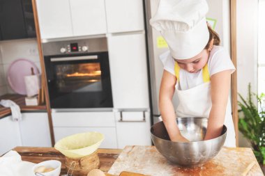 Küçük bir kız diz çöküp kurabiye yapıyor. 