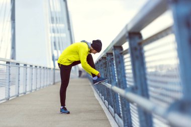 Genç sporcu güneşli kış gününde köprüde koşmadan önce kaslarını esnetiyor.