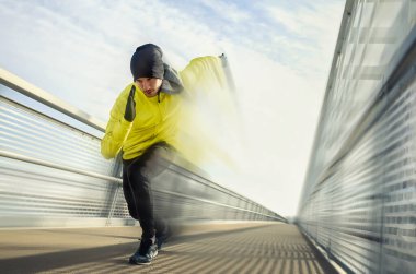 Çekici formda bir adam büyük ve modern bir köprü boyunca hızla koşuyor. Egzersiz, koşu, spor, kış. Erkek sporcu.