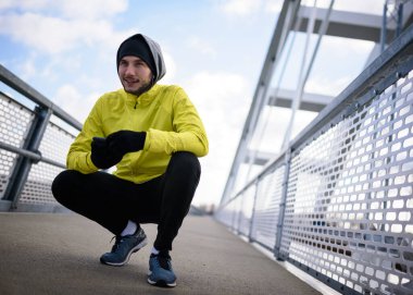 Yağmurlu bir günde egzersiz yapmaya hazırlanan rüzgarlık giymiş genç bir sporcunun portresi.