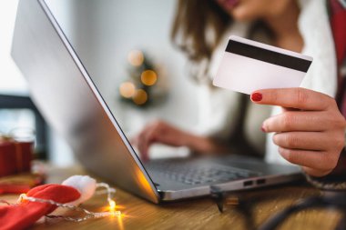 Evde dizüstü bilgisayar kullanan genç bir kadın online alışveriş yapıyor.