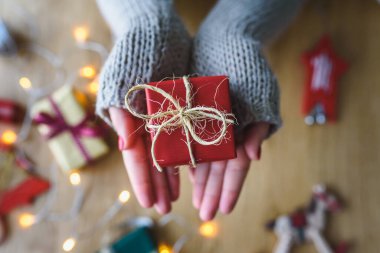 Kadın elleri ahşap arka planda Noel hediyesini tutuyor. 