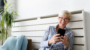 Neşeli olgun kadın evde telefon kullanıyor.