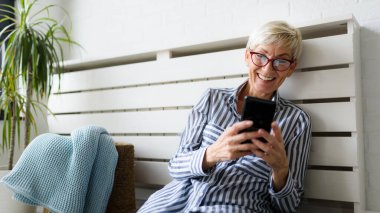 Neşeli olgun kadın evde telefon kullanıyor.