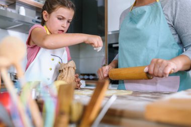 Önlüklü genç anne ve kız mutfakta birlikte yemek pişiriyorlar.