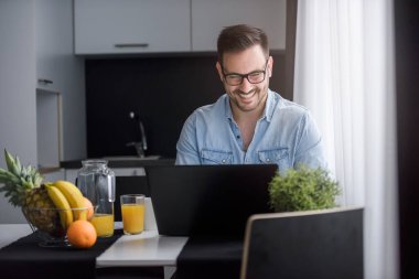 Bilgisayarlı genç adam mutfaktan çalışıyor.