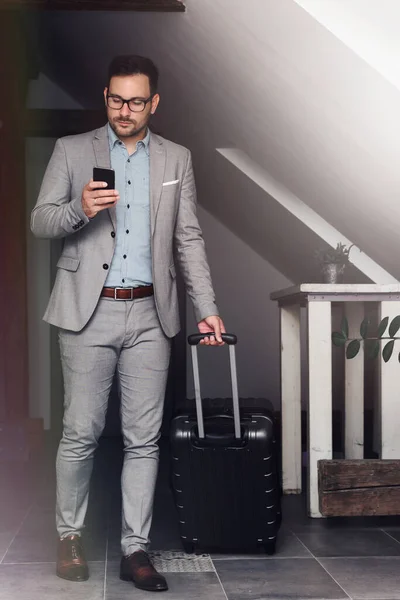 Elegant businessman with luggage in his hotel using smartphone.Traveling for work.